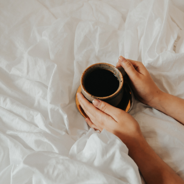 Woman holding a cup of coffee on top of her bed to wake up and be productive in the morning