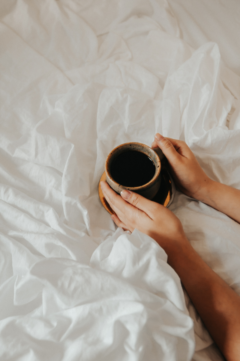 Woman holding a cup of coffee on top of her bed to wake up and be productive in the morning